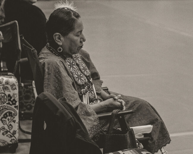 Woman in regalia sits with her eyes closed (Hunter George/The Vista)