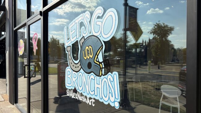 Artwork by Alex Nash is pictured on the storefront window of Roxy's Icecream and Social. The Artwork features a football helmet, horseshoe and "Let's Go Bronchos!" in blue letters. 