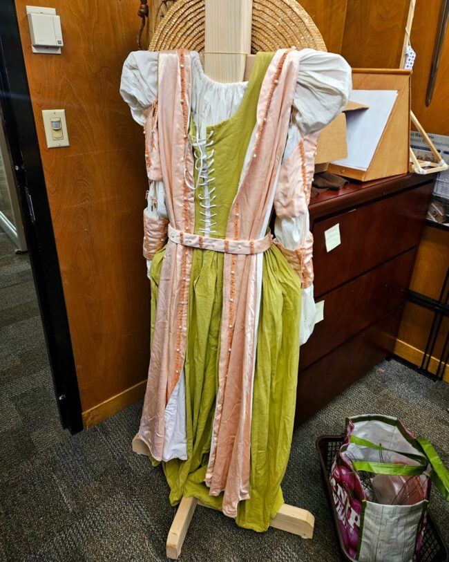 A green and pink dress is stationed to display a medieval prop.