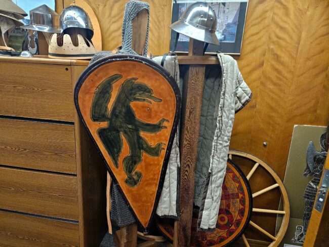 A metal helmet and shield with an emblem is stationed to display a medieval prop.