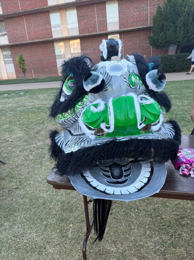 A black and green Chinese Dragon Head is displayed on a table with its mouth a-wide.