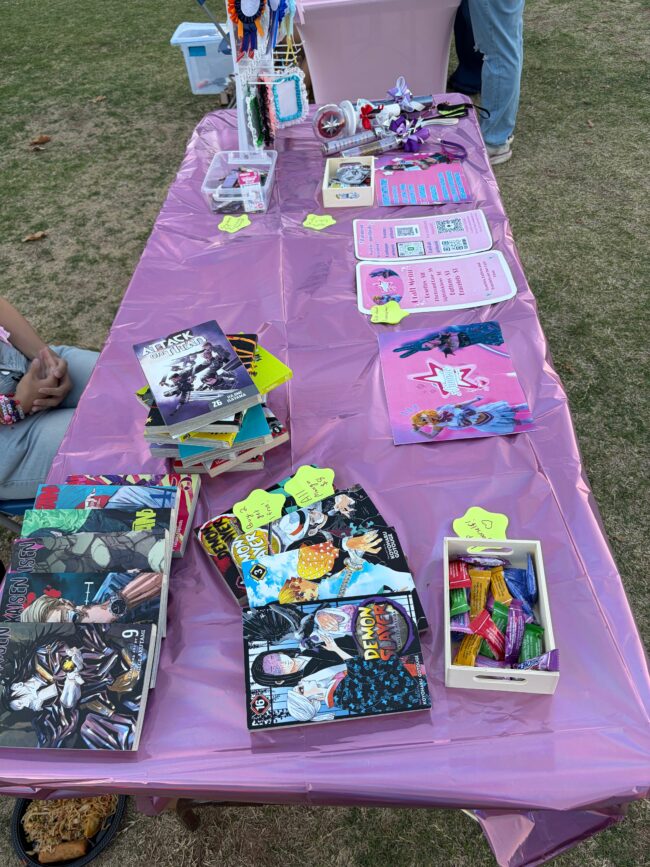 A purple booth has various anime mange books for sale, along with advertisements for Cosplay commissions.